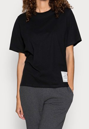 Czarna bawełniana koszulka z luźnym krojem. Posiada krótkie rękawy i metkę po lewej stronie. Zestawiona z szarymi spodniami.
