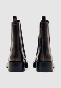 Rudos odinės aulinės botai su elastingomis šoninėmis panelėmis, liekna forma, švelni tekstūra ir mažu sustiprintu kulnu. Minimalistinis dizainas, be matomų detalių.