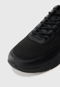 Black sneaker featuring a combination of leather and fabric materials, with a rounded toe, lace-up design, and visible stitching details.