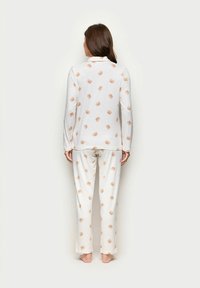 Langärmeliger weißer Schlafanzug mit einem wiederholten Muster aus hellbraunen Bärenköpfen, weichem Stoff und entspannter Passform sowie geraden Hosen.