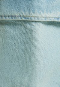 Světle modrá džínová látka s hladkým, strukturovaným povrchem. Obsahuje viditelné švy a mírný lesk, což ukazuje na klasický design džínů.