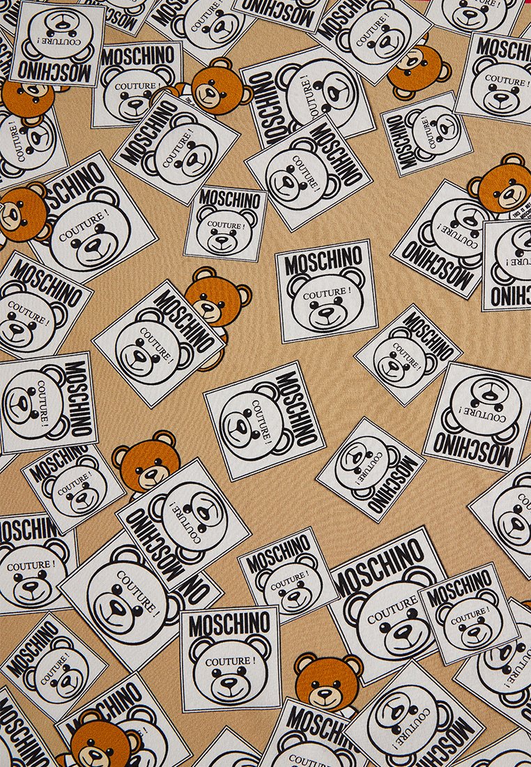 Stoff mit einem wiederholten Muster von Teddybär-Grafiken und dem Text "MOSCHINO COUTURE!" in Schwarz und Orange auf einem beigefarbenen Hintergrund.