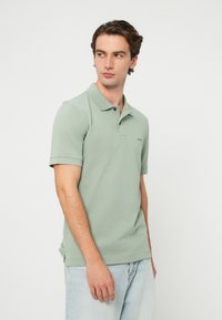 Zielona bawełniana koszulka polo z krótkimi rękawami, zapinana na trzy guziki i z subtelnym logo marki na lewej piersi. Lekko teksturowany materiał.