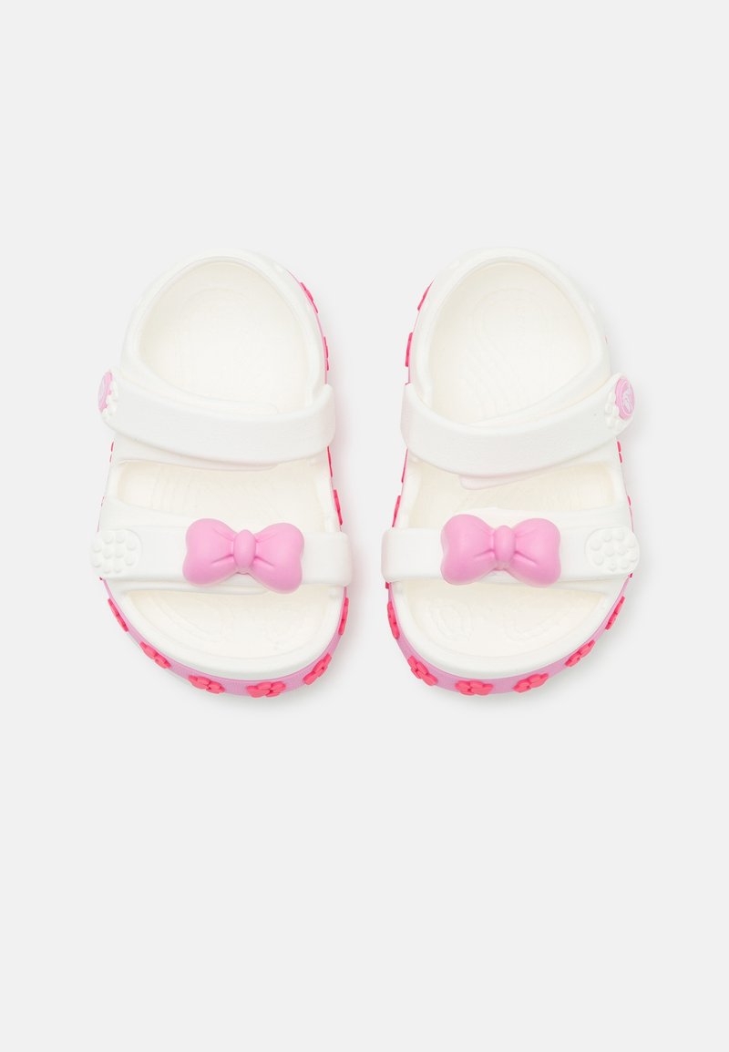 Sandales blanches pour enfants avec brides ajustables, nœuds roses sur les brides avant et motifs floraux roses sur les semelles.