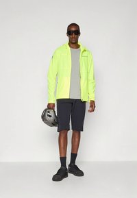 Neon gul jacka med hög synlighet, grå tröja, marinblå shorts, svarta sneakers och hjälm; texturerat tyg, atletisk passform, funktionell design.