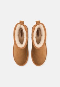 Botas de ante marrón con forro beige suave, puntera redondeada y tiradores de tela en el tobillo. Textura suave y diseño sencillo.