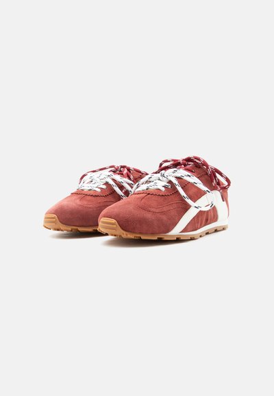 Paire de baskets en daim rouge avec des bandes latérales blanches, des lacets à motifs blancs et rouges, et des semelles en caoutchouc naturel sur fond blanc.