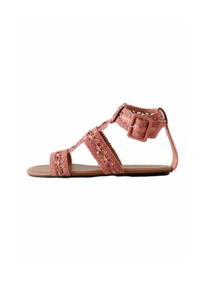 Lapos rózsaszín szandál szőtt virágos pántokkal, nagy csattal és hátul pánttal, laza viseletre tervezve.