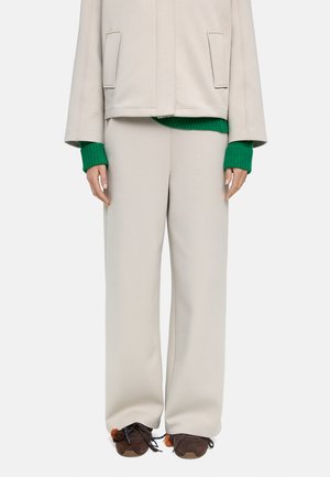 Beżowe szerokie spodnie zestawione z kremową kurtką na zielonym swetrze oraz brązowe trampki z pomponikami na sznurówkach.