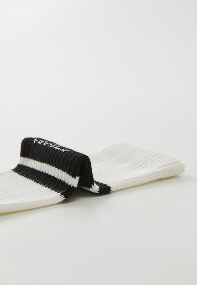 Chaussettes blanches avec une texture côtelée, dotées d'un revers rayé noir et blanc. Bout arrondi et détail de couture contrasté.