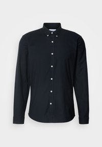 Chemise noire à manches longues à boutons avec col à boutons et boutons blancs, présentée sur un fond clair uni.
