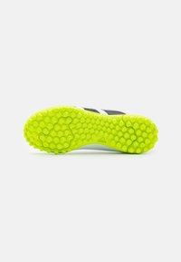 Scarpa da calcio nera con suola in gomma gialla brillante e texture, caratterizzata da motivi esagonali e dettagli bianchi lungo i lati.