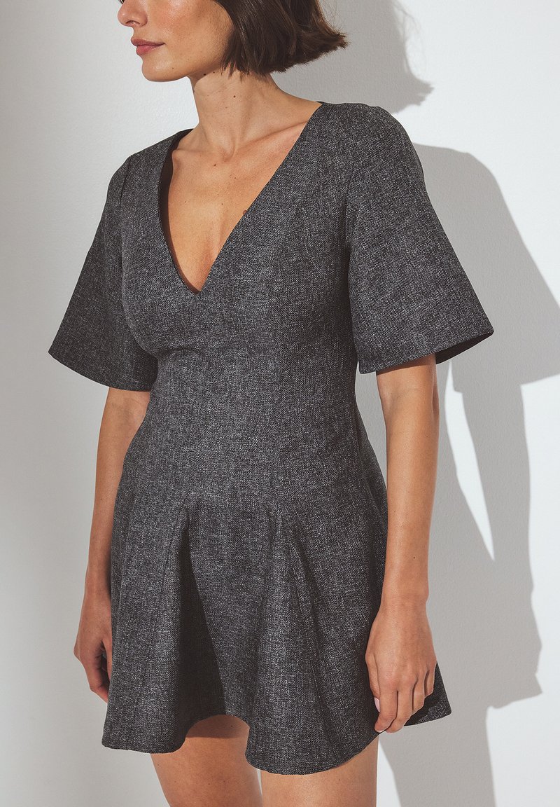Hallikseni hall dress, mis on valmistatud tekstureeritud kangast, sügava V-kaelusega ja lühikeste, laiendatud varrukatega, sobitatud korpusega ja volangiga seelikuga.