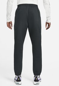 Mörkgrå cargobyxor i sweatshirtmaterial med elastiskt midjeband, muddar vid anklarna, sidoficka på vänster sida och en slät yta.