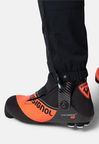Botte de ski noire et orange avec des accents en carbone, dotée d'un design épuré, d'une surface texturée et de marquages sur le côté.