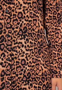 Camicia con stampa leopardata in arancione e nero, con chiusura a bottone, texture liscia e motivi animali distintivi.
