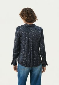 Mørkeblå leopardmønstret bluse med lange ærmer, krave og knapdetaljer ved manchetterne. Blødt, glat stof med en afslappet pasform.