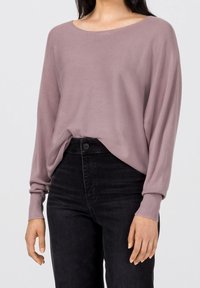 Pullover à manches longues, ample, en tricot mauve doux avec un large col rond et des poignets côtelés, porté sur un jean noir taille haute.