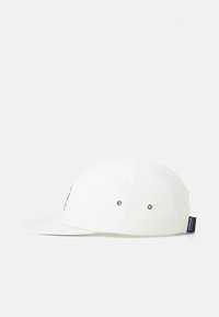 Hvit fem-panelets caps med flat skjerm, metalløyelater på siden, og liten svart Patagonia-logo-merke på baksiden til høyre.