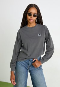 T-shirt en coton gris à manches longues avec un col rond et un petit patch logo sur la poitrine, associé à un jean bleu taille haute.
