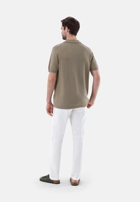 Polo shirt a maglia di un verde oliva chiaro, maniche corte, colletto a coste, abbinato a pantaloni bianchi e sandali scuri. Texture liscia, design casual.