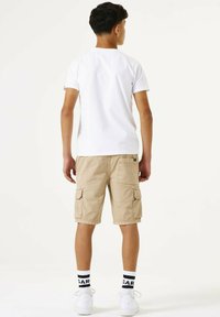 Witte t-shirt met korte mouwen en ronde hals, gecombineerd met beige cargoshorts met zijzakken, gedragen met witte sneakers en gestreepte sokken.
