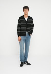 Black and gray striped knit cardigan with a V-neck and button closure, paired with light blue jeans and black sneakers.
