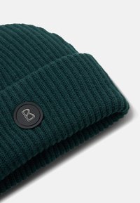 Donkergroene gebreide beanie met ribbelstructuur en een omgeslagen boord. Bevat een ronde zwarte logopatch met een letter "B" in zilver.