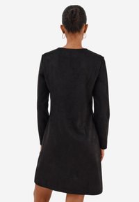 Černé semišové šaty s dlouhými rukávy, kulatým výstřihem a mírně rozšířeným lemem. Hladká textura s minimalistickým designem.