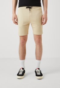 Beige bomuldsbukser med elastisk talje, snor og sidelommer. Har en tætsiddende pasform og en glat tekstur.