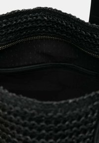 Borsa a rete nera con una superficie texture, dotata di una tasca con zip all'interno e di una fodera in tessuto liscio.