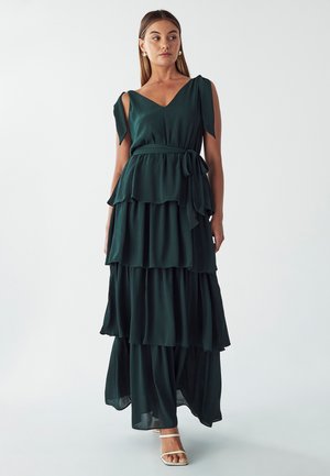 Tiered dark green maxi dress in lightweight fabric, featuring a V-neckline and shoulder ties, with a belted waist and flowing hem.