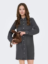 Grijs denim overhemdjurk met lange mouwen, knoopsluiting, twee borstzakken en een losse pasvorm. Model houdt een bruine handtas vast.