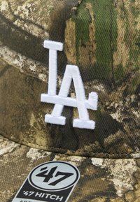 Καμουφλάζ καπέλο με λευκό κεντημένο λογότυπο "LA". Υφασμάτινη υφή με γήινους τόνους, που διαθέτει ελαφριά γυαλάδα και καμπύλο γείσο.