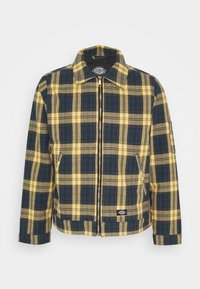 Kostkovaná bunda v žluté a tmavě modré barvě, se zapínáním na zip vpředu, špičatým límečkem a bočními kapsami. Vyrobená z texturované látky.