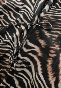 Črno-bež tkanina z vzorcem zebra, s trakovami okoli vratu in nabranimi teksturami po vsej površini.