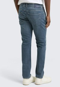 Männerblaue Jeans aus Denim mit gerader Passform, ausgestattet mit zwei Gesäßtaschen und dezenten Nähdetails, kombiniert mit weißen Turnschuhen.