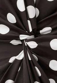 Czarna tkanina skręcona na środku z dużymi białymi kropkami równomiernie rozmieszczonymi na materiale.