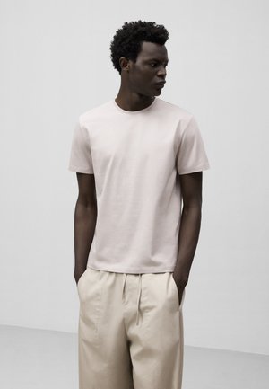 Light pink cotton t-shirt with a crew neck and short sleeves, paired with beige wide-leg trousers, showcasing a smooth texture.