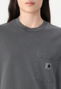 T-shirt in cotone grigio con collo rotondo, dotato di una tasca sul petto sinistro e un piccolo logo. Texture liscia con dettagli di cuciture curate.