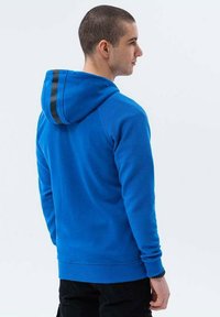 Sudadera azul con un patrón texturizado y acanalado. Presenta una capucha y puños de rayas negras en contraste, y un ajuste relajado.