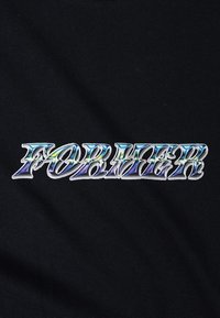 Juodas audinys su blizgiu, rūdytu „FORMER“ logotipu stilizuotu šriftu, pasižymintis lygiu tekstūru ir kreivomis raidėmis.