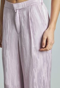 Helle rosa Schlaghosen mit strukturiertem Oberflächenmaterial, die dezente vertikale Streifen und ein Vorderfalte-Detail aufweisen.