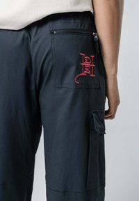 Czarne spodnie cargo z zamykaną na zamek kieszenią i czerwonym wyszywanym detalem. Charakteryzują się trwałym materiałem, bocznymi kieszeniami oraz luźnym krojem.