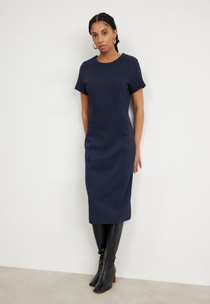 Navy fitted dress with short sleeves, rounded neckline, and seam detailing. Paired with knee-high black boots. Smooth texture.