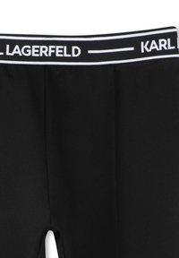 Leggings noirs avec une ceinture élastique blanche, portant le logo "KARL LAGERFELD". Texture lisse et coupe ajustée, idéales pour un usage décontracté.