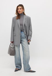 Pelēks pārāk liels žakets ar ielocītām atlokām, apvienots ar pieguļošu turtleneck un platajām gaiši zilo džinsu biksēm. Pelēka rokassoma un norādītas kurpes.