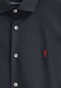 Camicia button-up blu navy in tessuto liscio con colletto classico. Presenta bottoni argentati e un logo ricamato rosso sul lato sinistro.