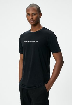 Sort bomulds t-shirt med korte ærmer og rund halsudskæring, med hvid tekst der står "DER KAN IKKE GØRES NOGET" tværs over brystet.