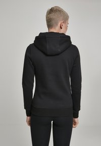 Black hoodie made of soft fabric with a ribbed hem and cuffs. Features a drawstring hood and smooth texture, showing the back view.